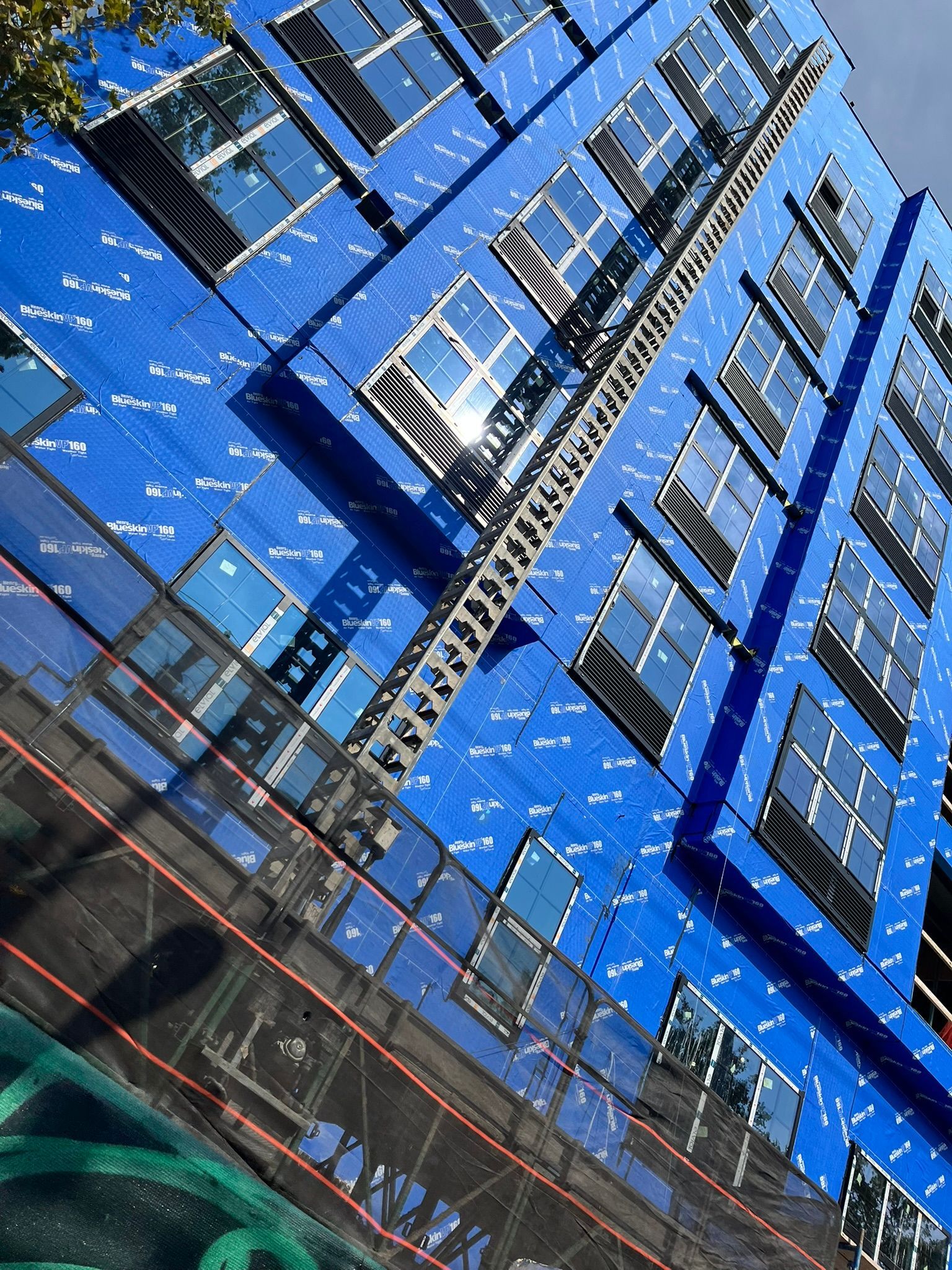 Blue modern building facade with many windows, viewed from below at a tilted angle.