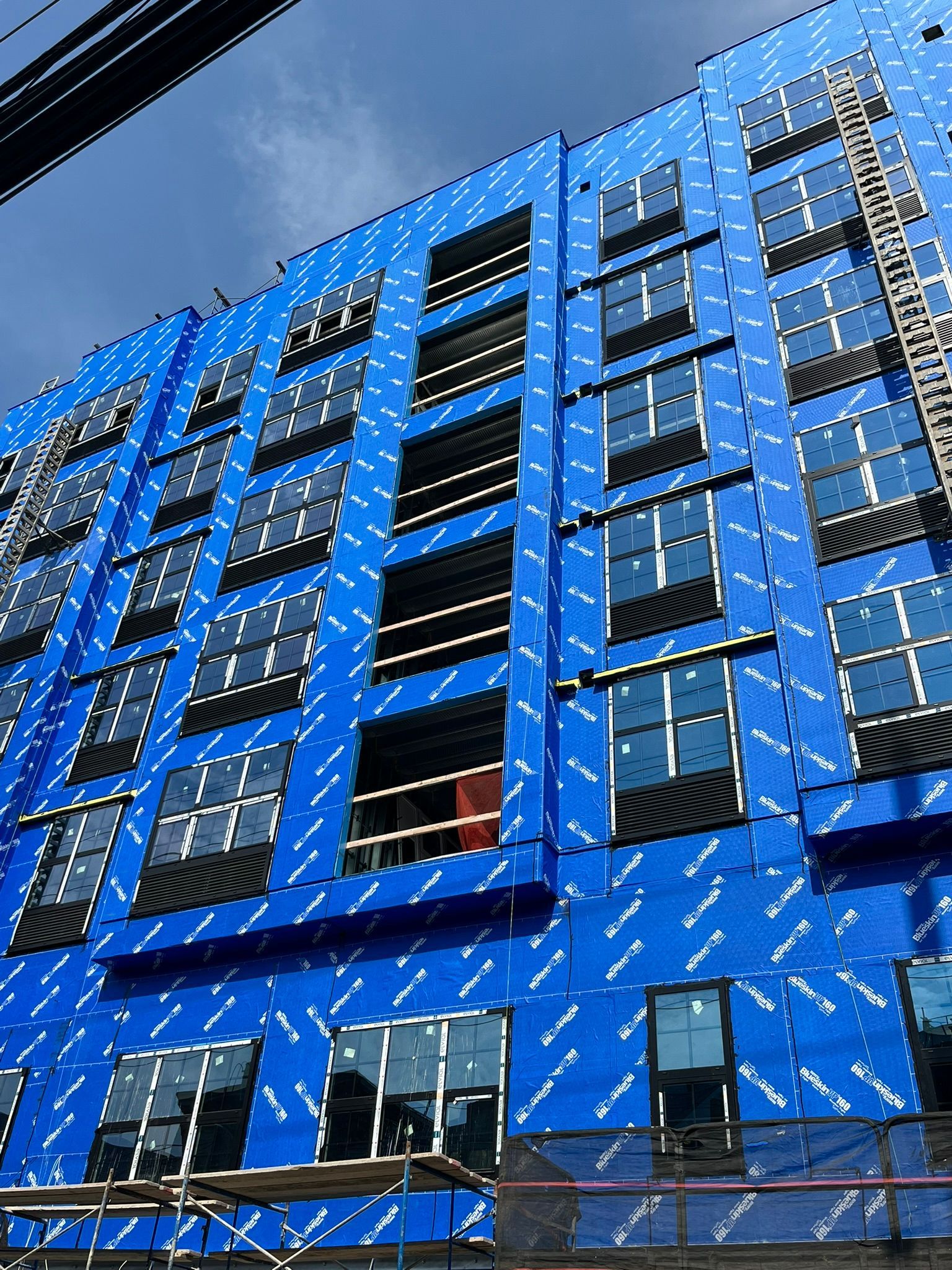Blue high-rise building under construction with rows of windows and scaffolding against a clear sky.