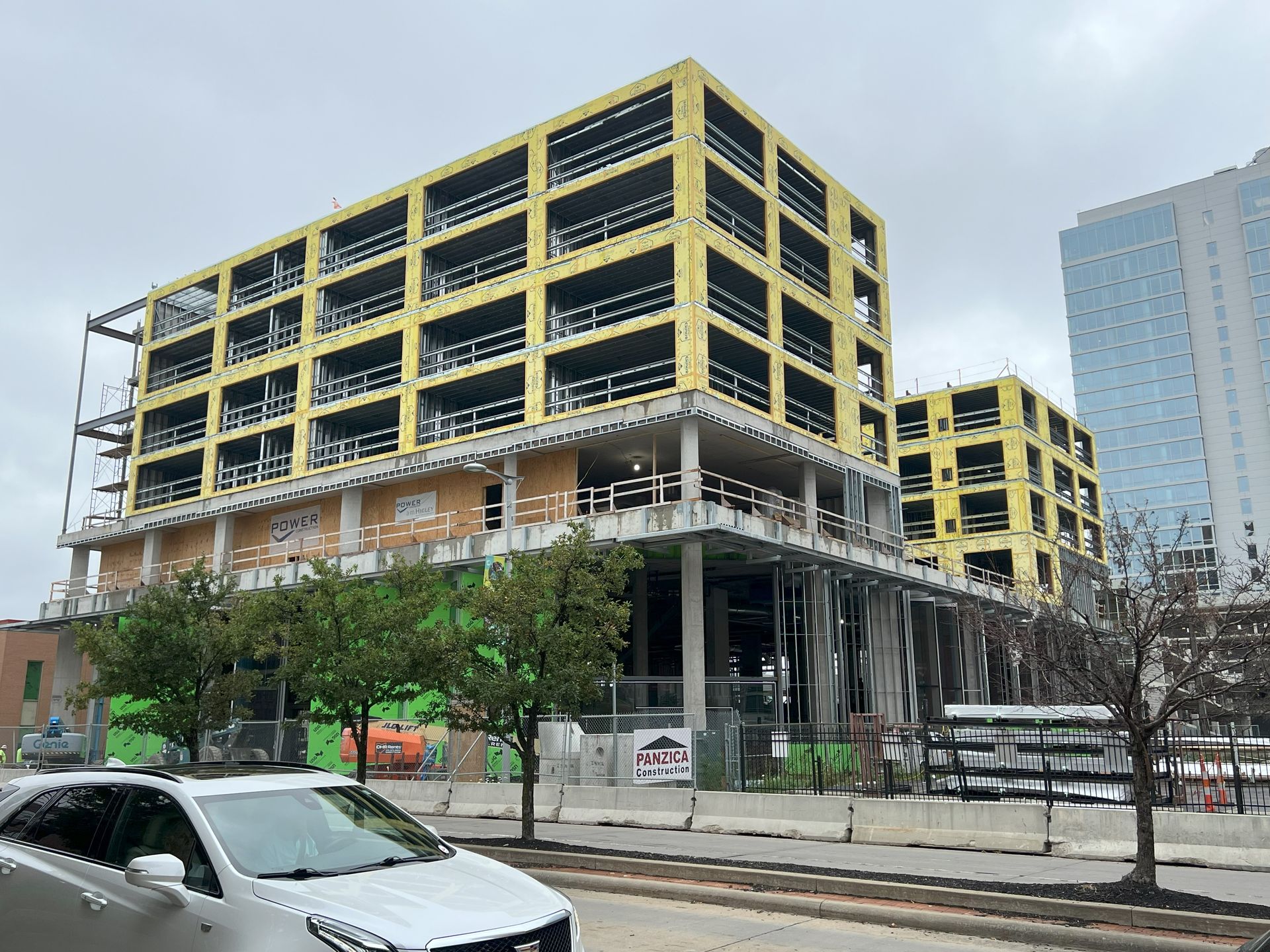 A white car is parked in front of a large building under construction.