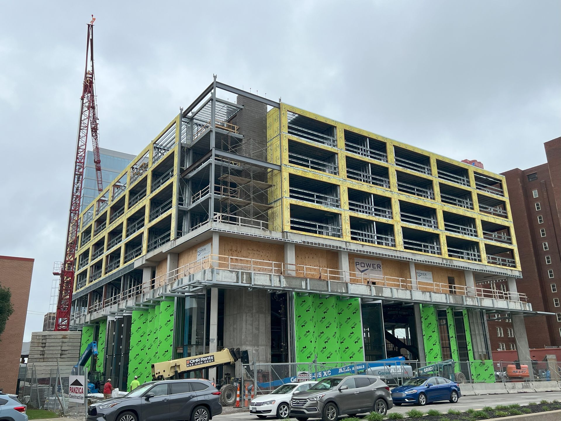 A large building under construction in a city with cars parked in front of it.