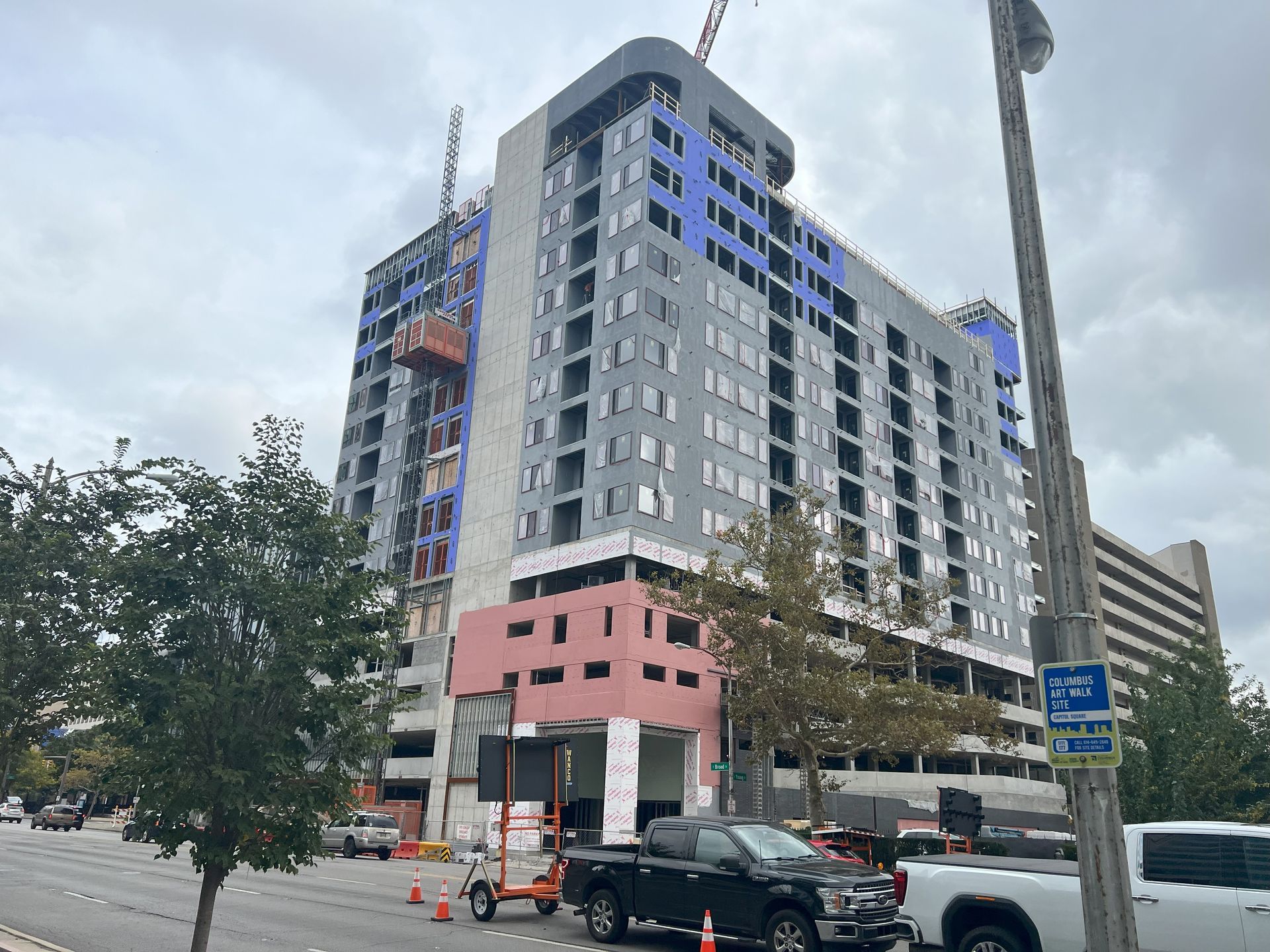 A large building is being built in a city with vehicles parked in front of it.
