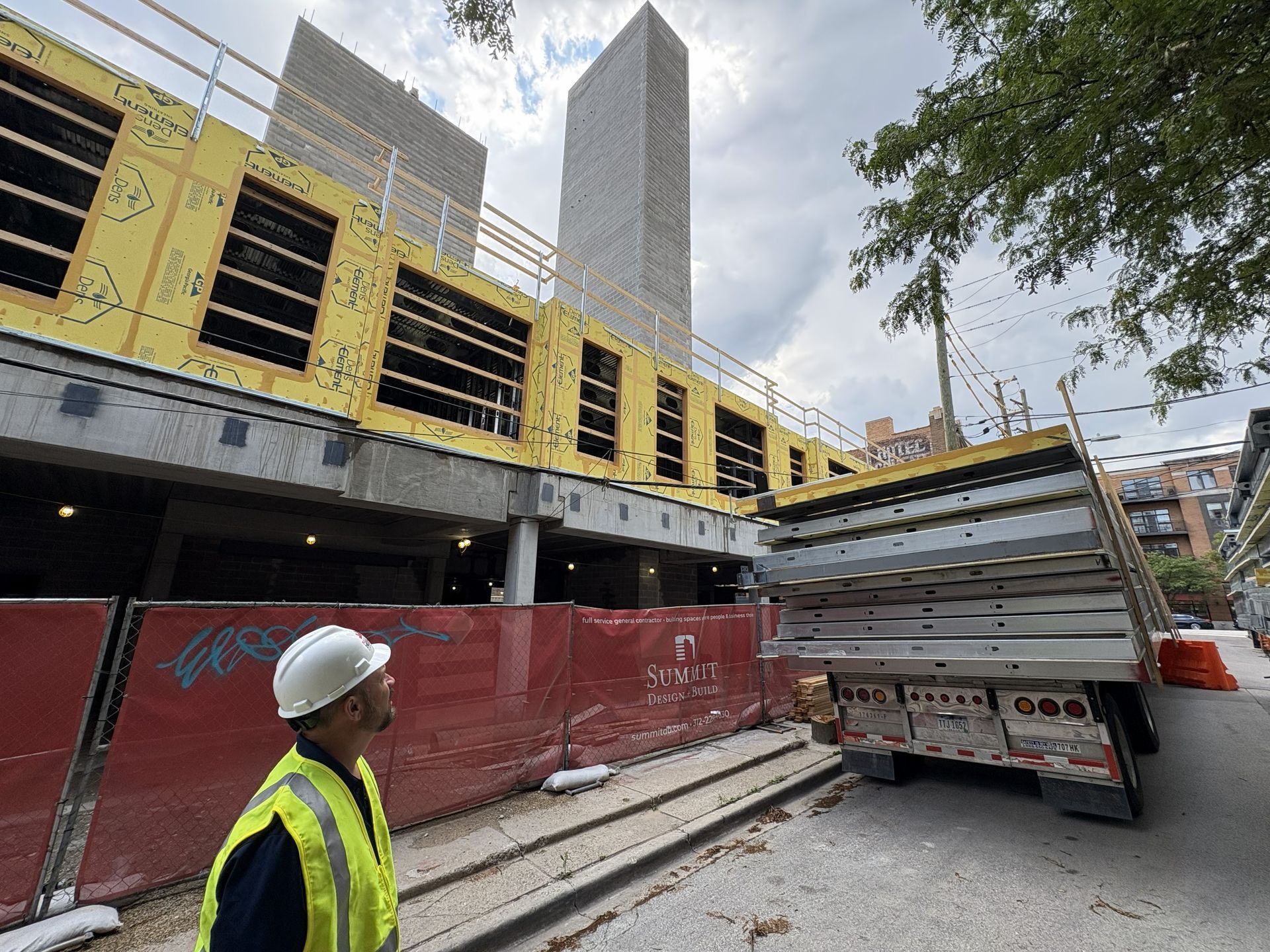 Construction site with worker in safety vest beside truck under a raised road deck.