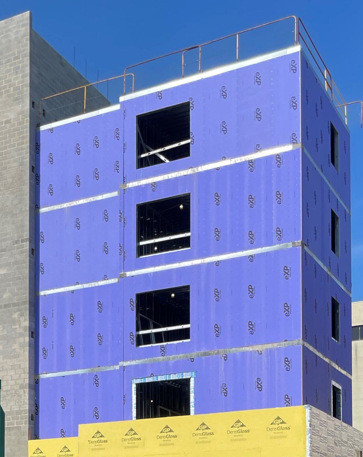 A building under construction with purple insulation sheets on the side.