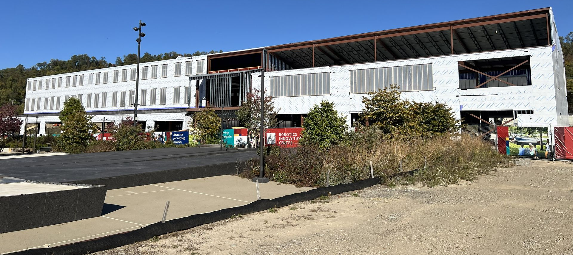 Wide view of a large building being built, debris, and a cleared foreground under blue sky.