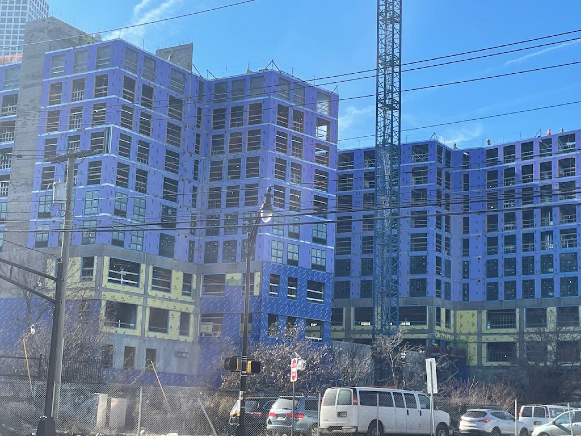 A large building is being built in a city with cars parked in front of it.