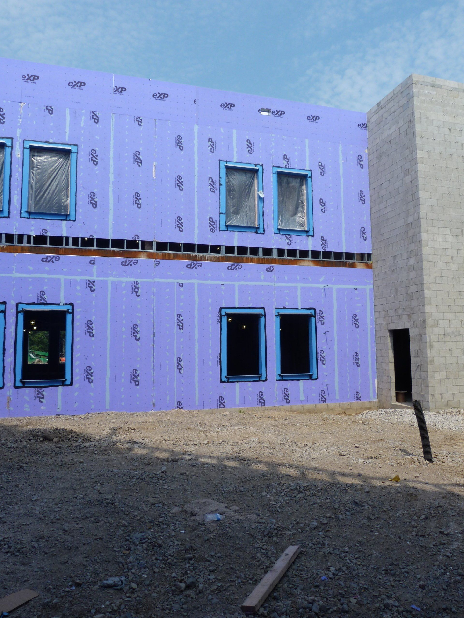A building under construction with purple insulation and blue windows.