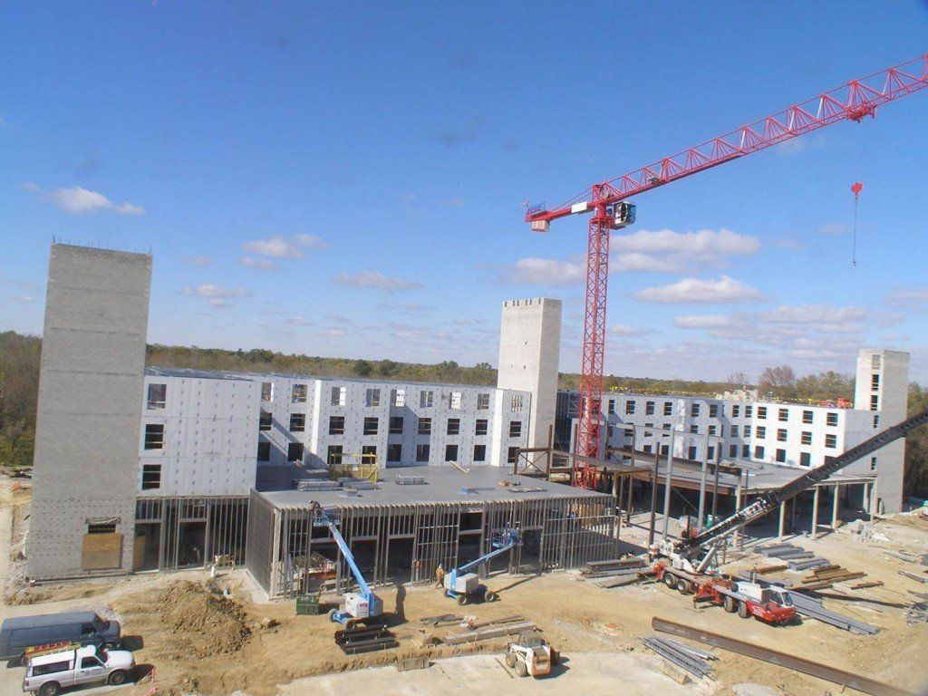 A large building under construction with a red crane in the foreground.