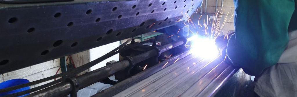 A man is welding a piece of metal in a factory.