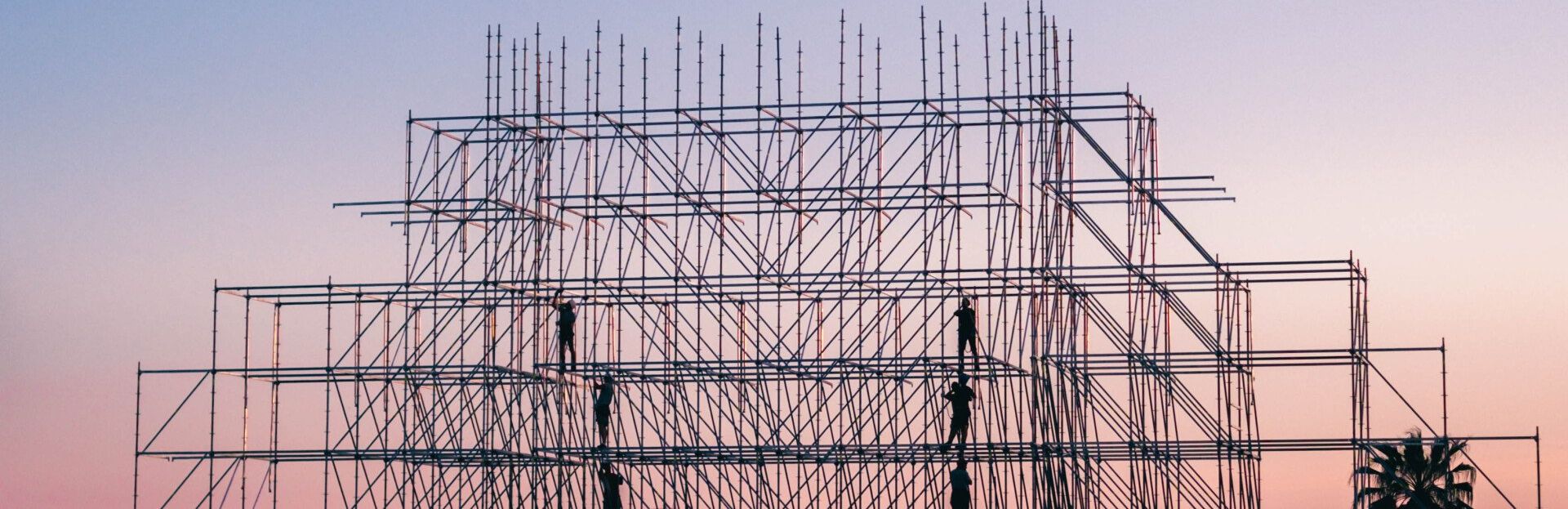 A building is being built with scaffolding and a sunset in the background.