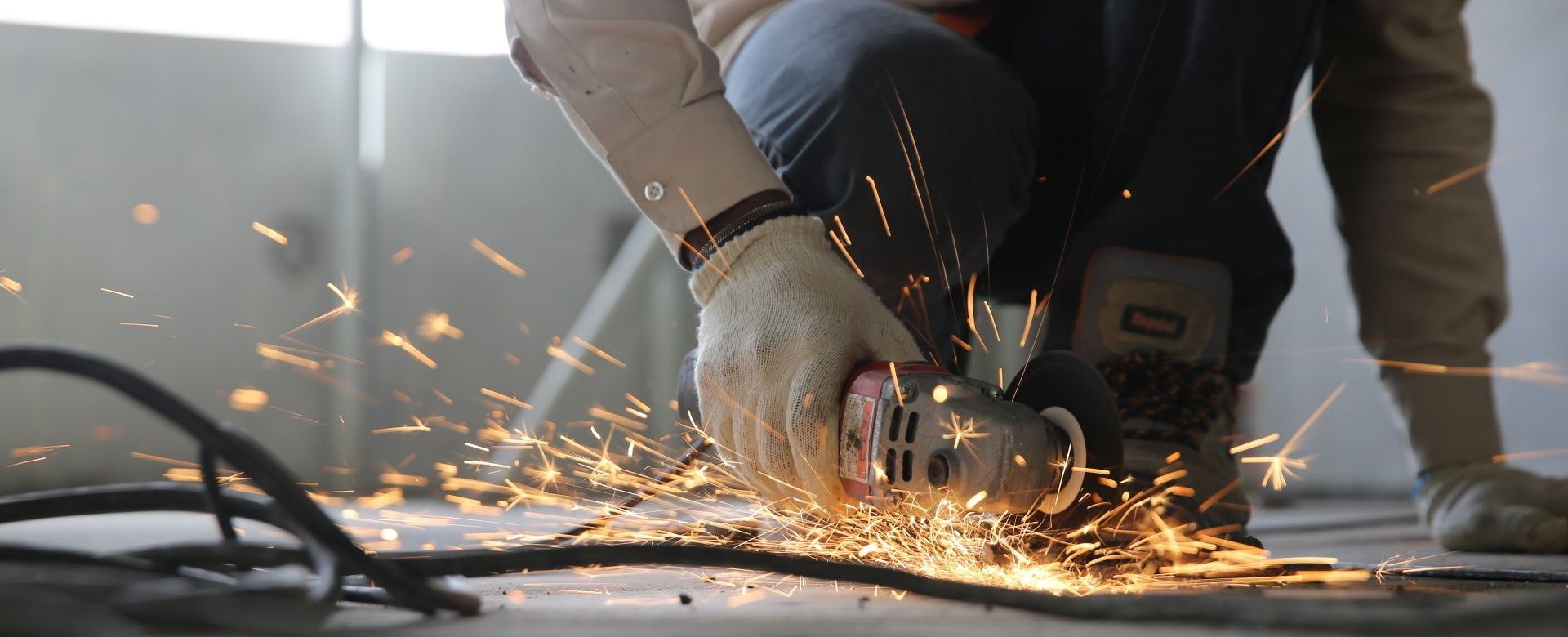 A man is using a grinder to cut a piece of metal on the floor.