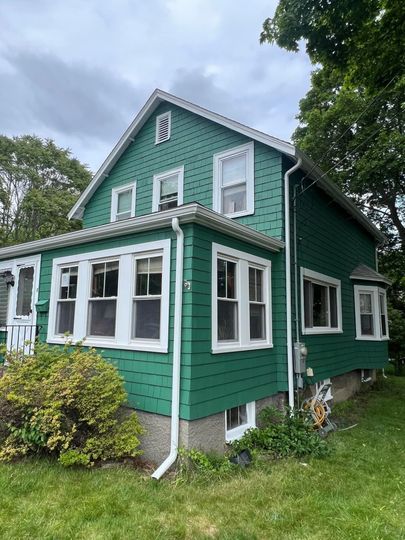 A green house with white trim and windows is sitting on top of a lush green field.
