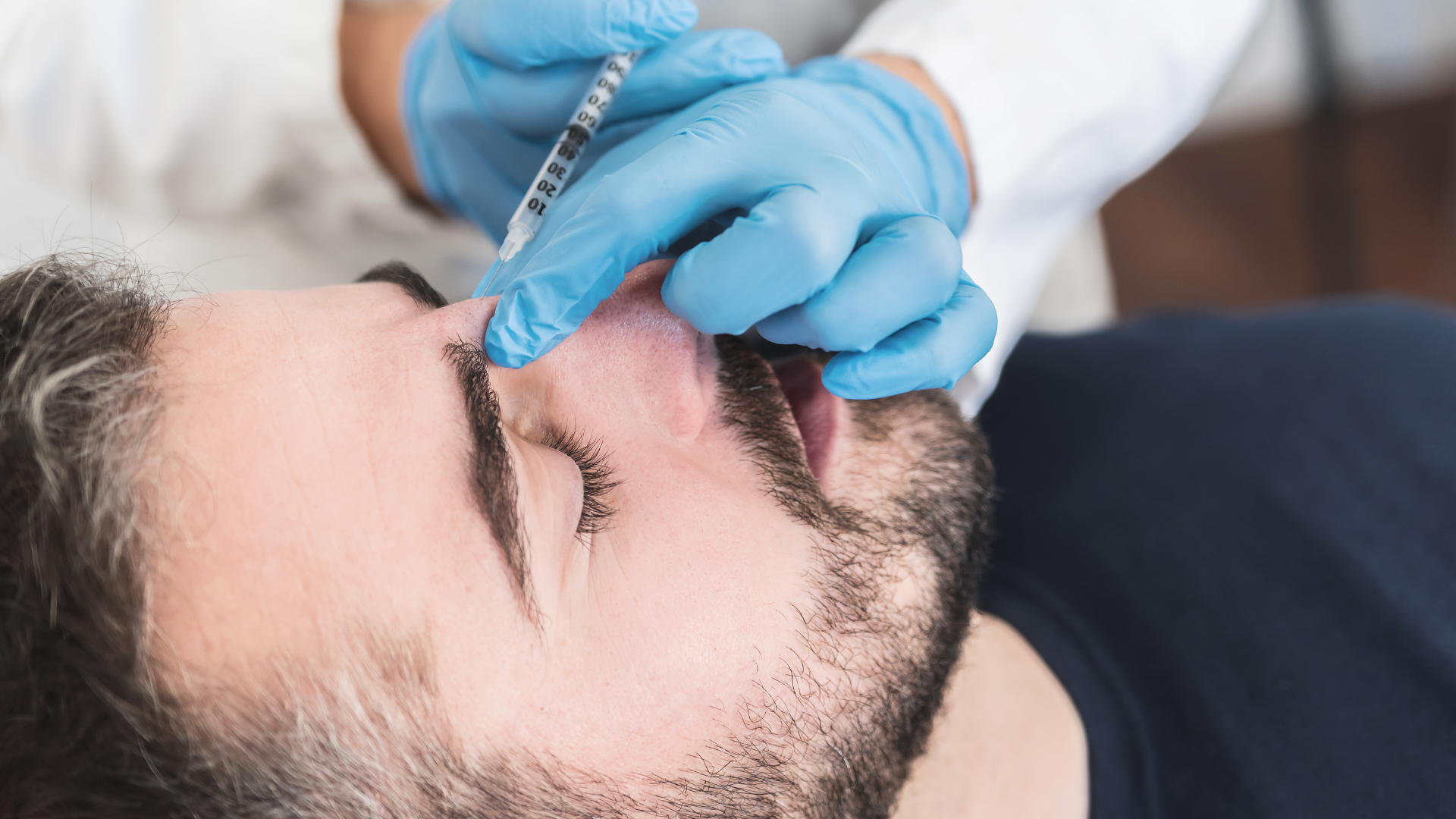 Gloved hand applying a nasal procedure to a reclining man in a clinical setting