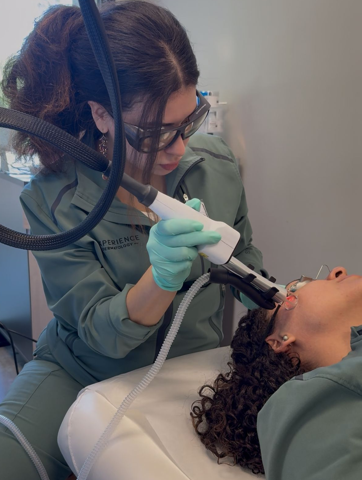 Dentist in teal scrubs using a dental tool to examine a patient in a chair