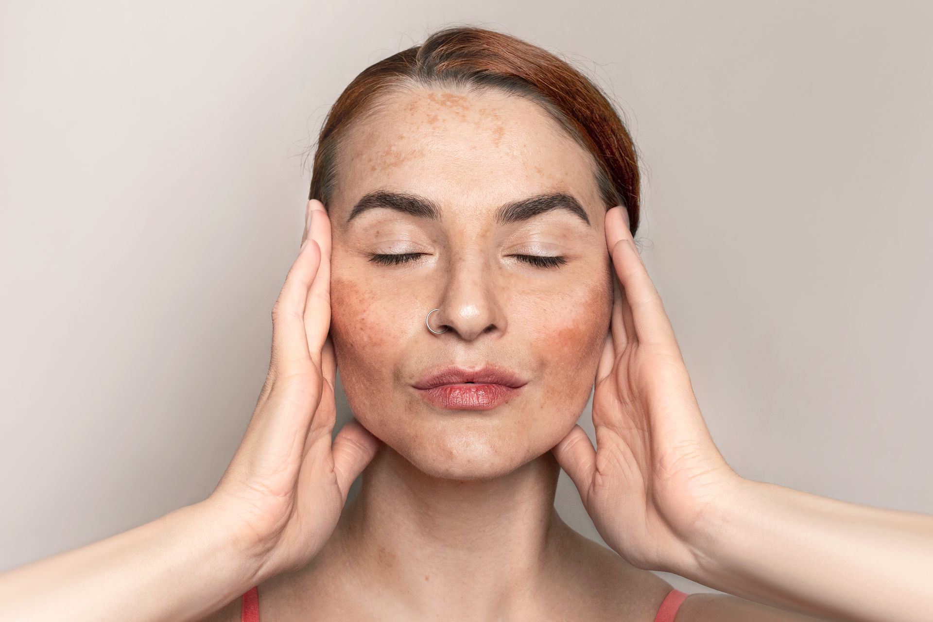 Person with closed eyes gently massaging temples against a plain beige background