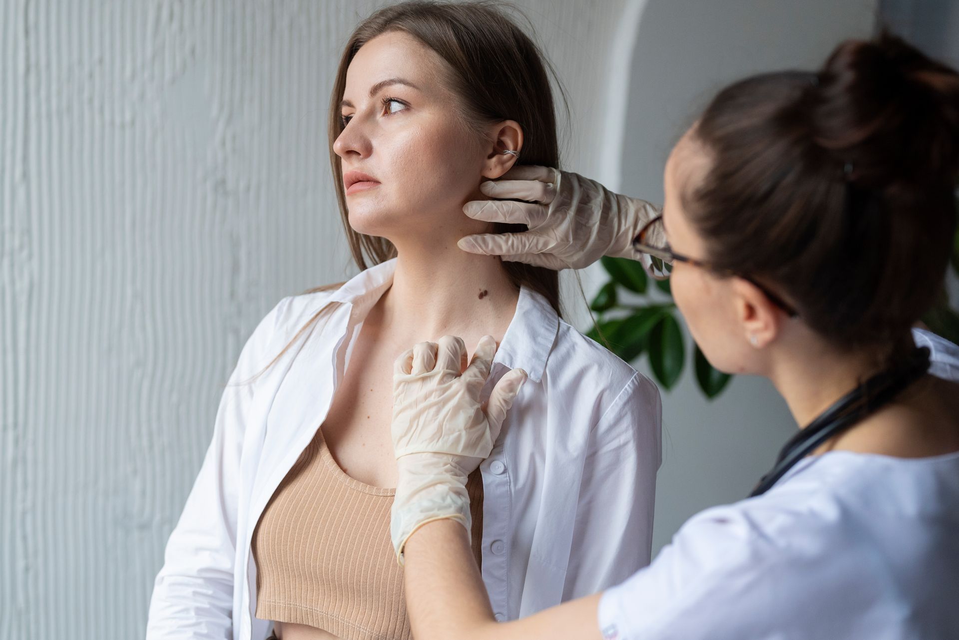 Healthcare worker examining a woman’s neck in a clinic, with the patient seated in profile.