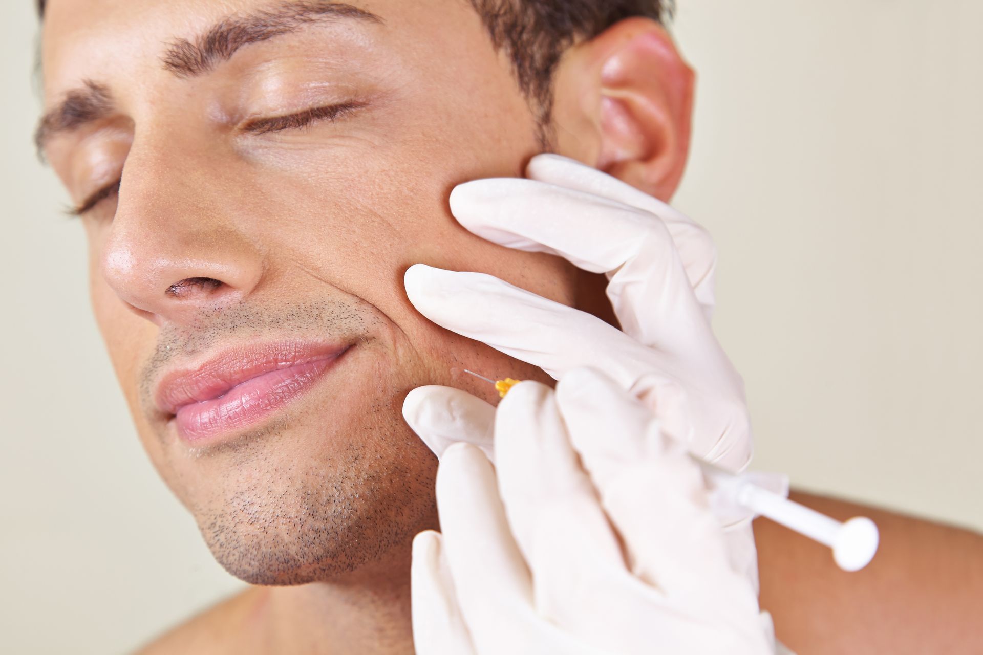 Cosmetician applying treatment to a man's cheek with gloved hands and a tool