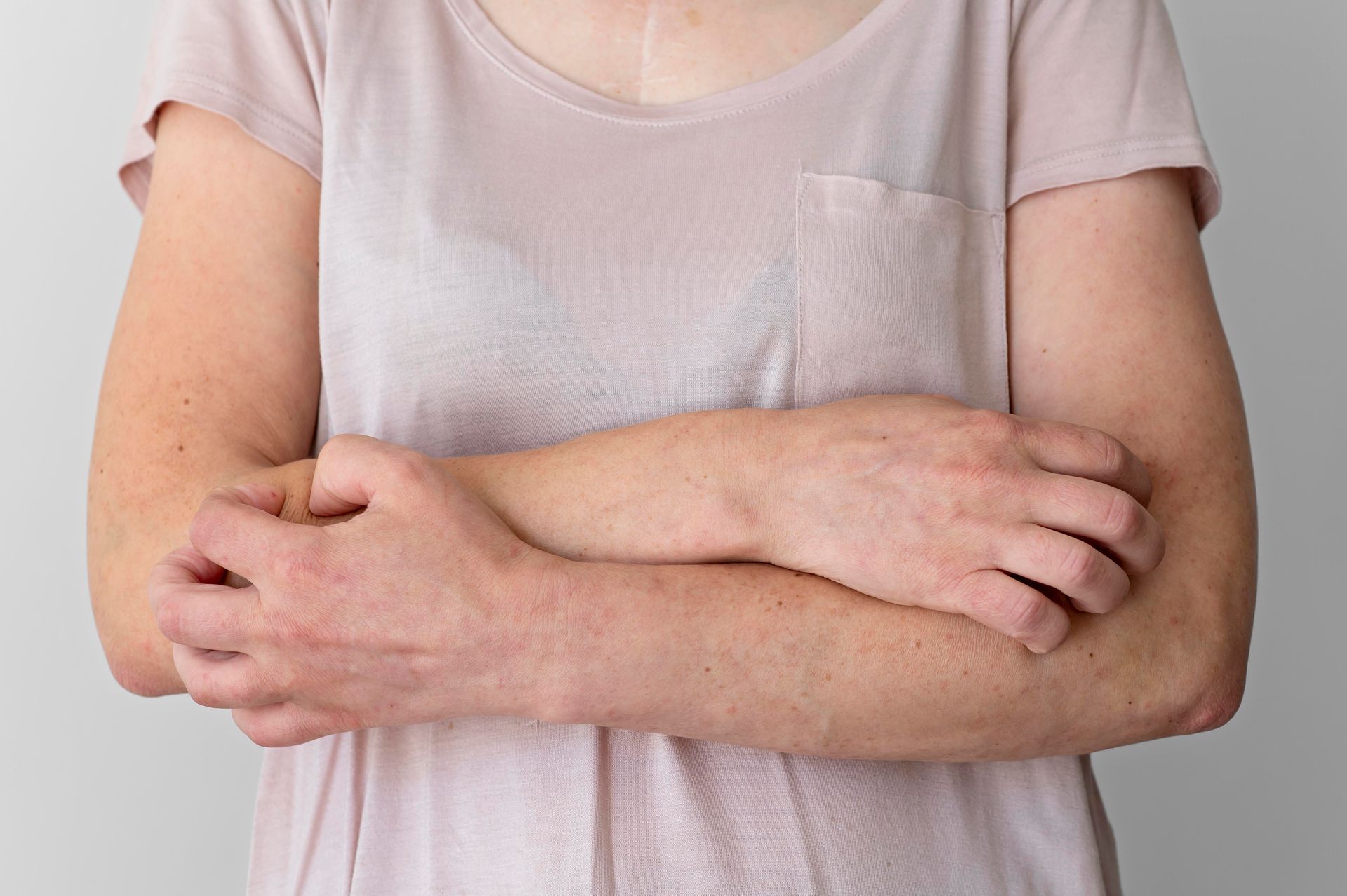 Person in a light pink shirt crossing arms over their chest against a plain background