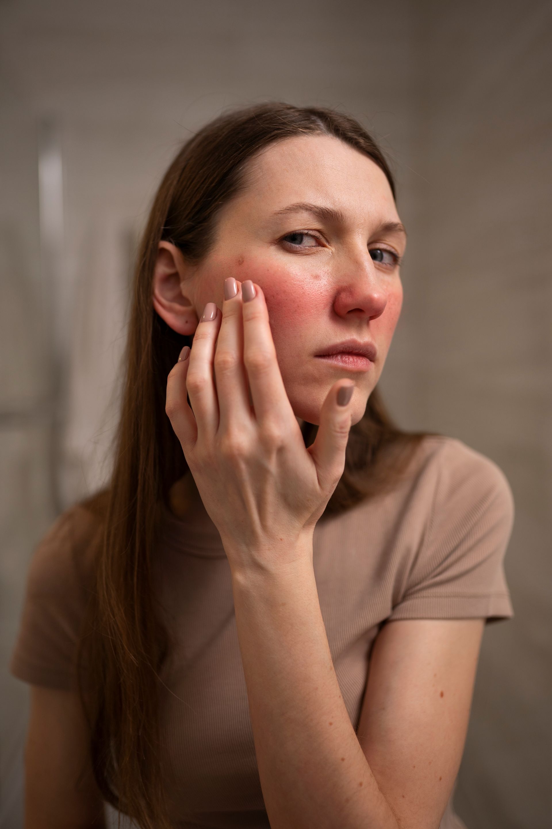 Close-up of a woman touching her red, irritated cheek against a neutral background