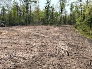 A large dirt field in the middle of a forest with trees in the background.