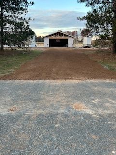 A dirt road leading to a garage with a white building in the background.