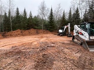 Two bulldozers are sitting in a dirt field in the middle of a forest.