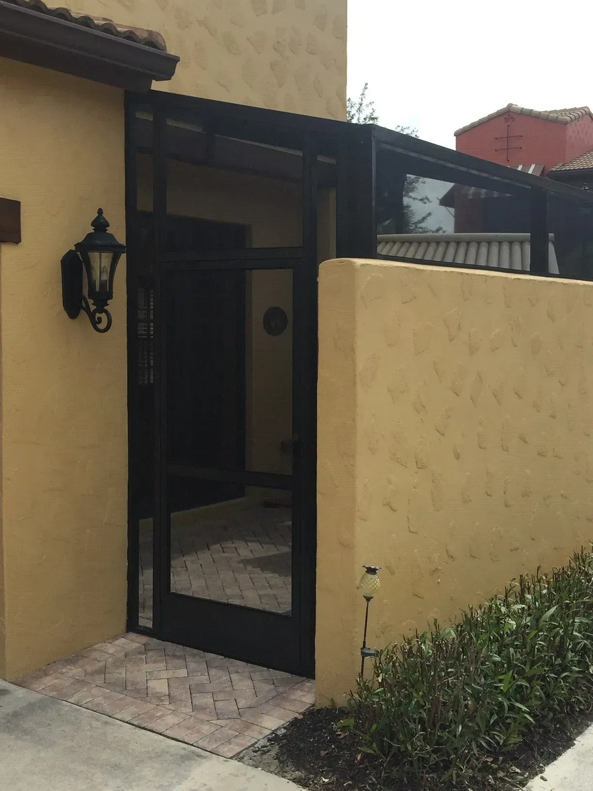 A yellow building with a black door and a lamp on the sidewalk