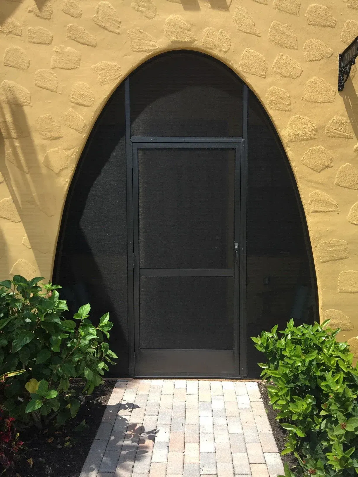 A black screen door is on the side of a yellow building.