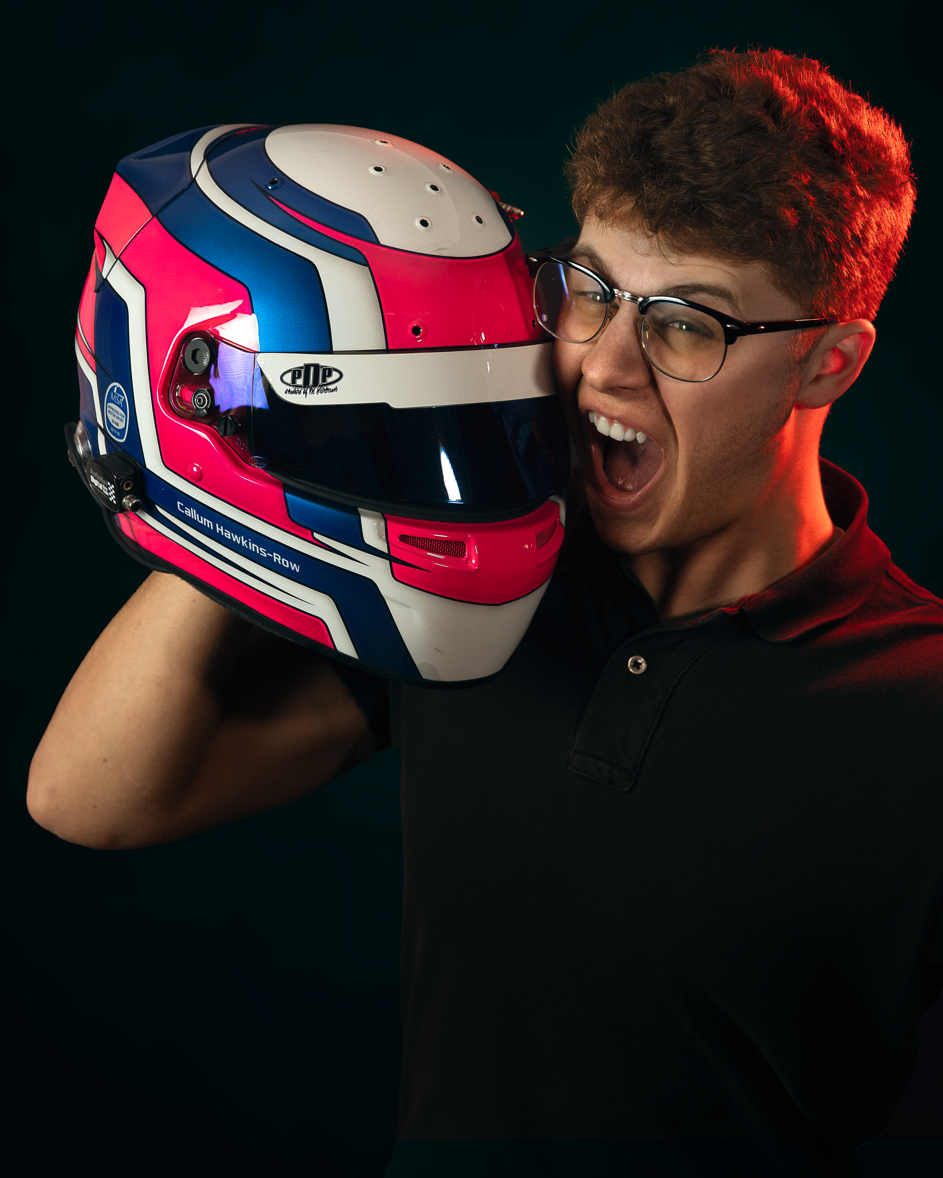 A young man wearing glasses is biting a racing helmet