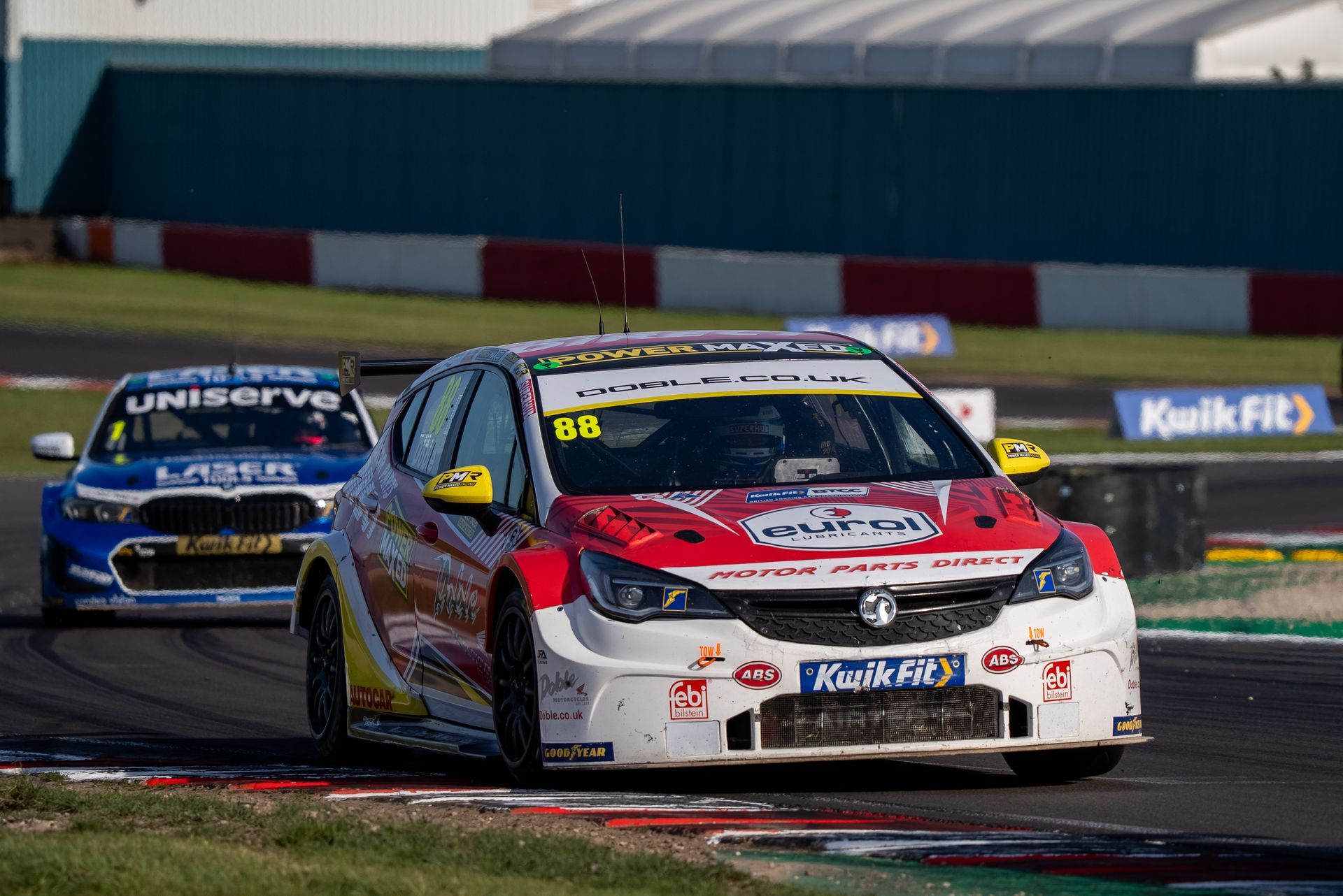Race car #98 (white/red/yellow) on track, followed by blue race car.