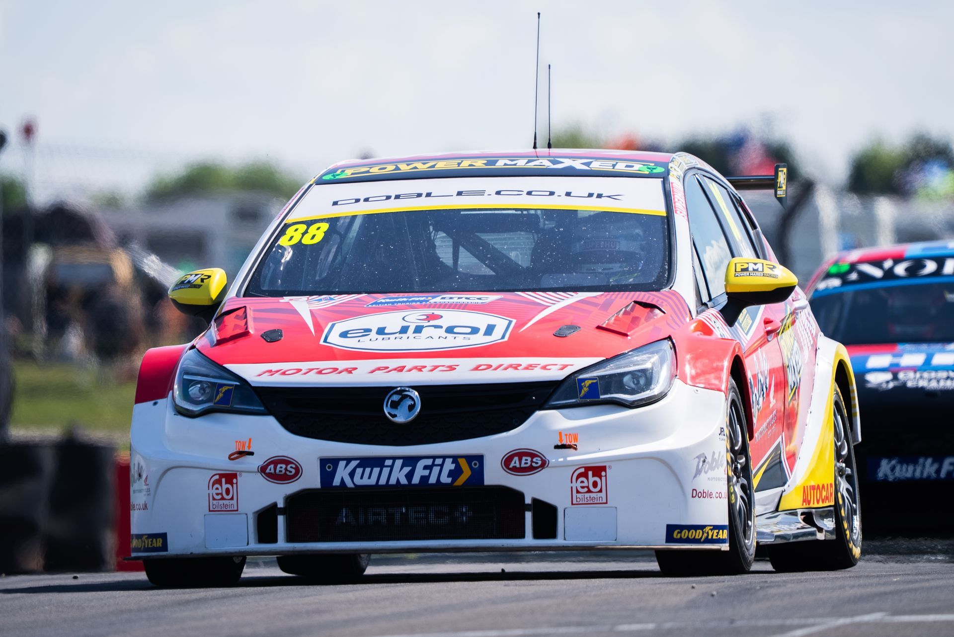 Race car, white and red with sponsor logos, on a racetrack, heading straight.