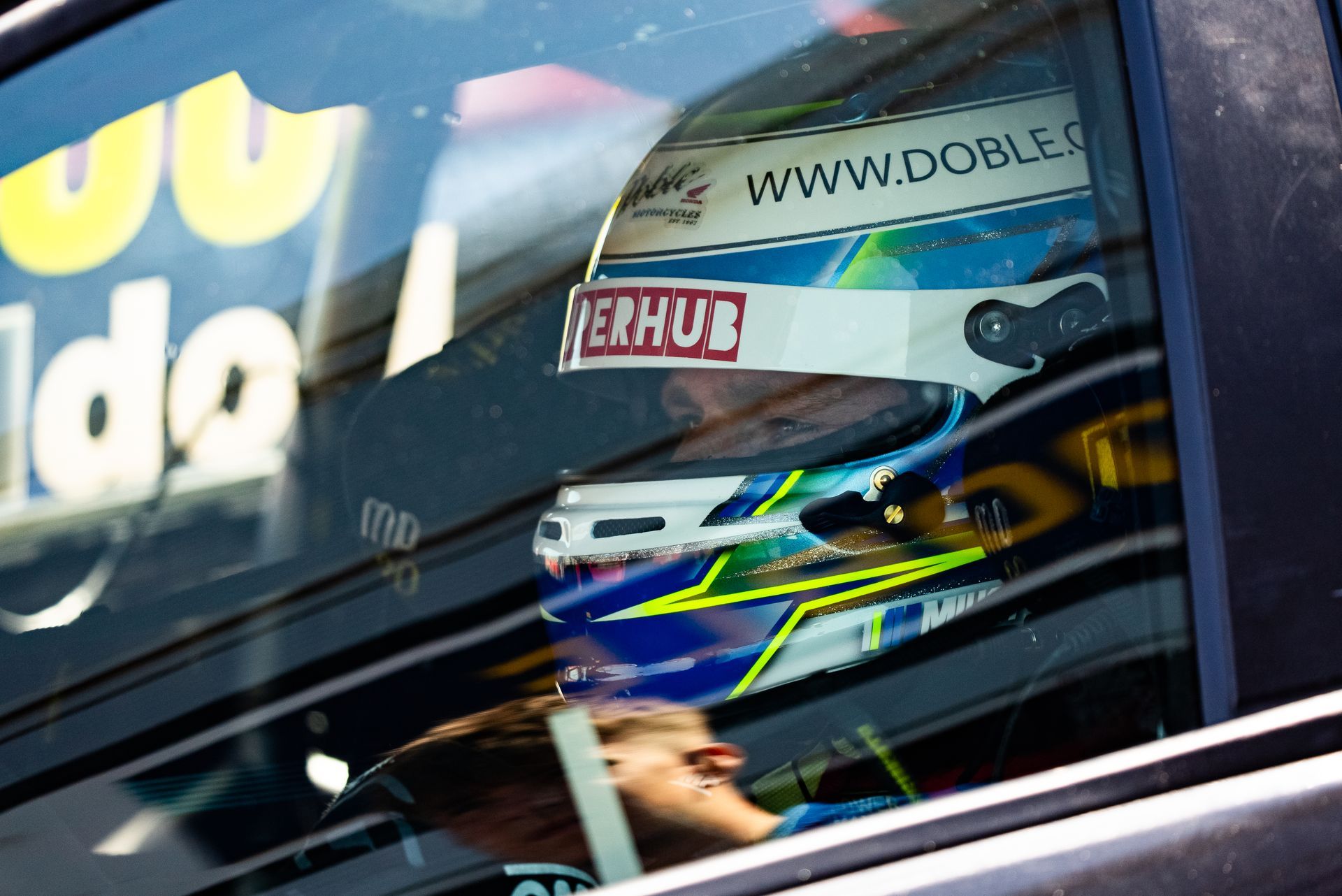Race car driver in helmet seen through car window.