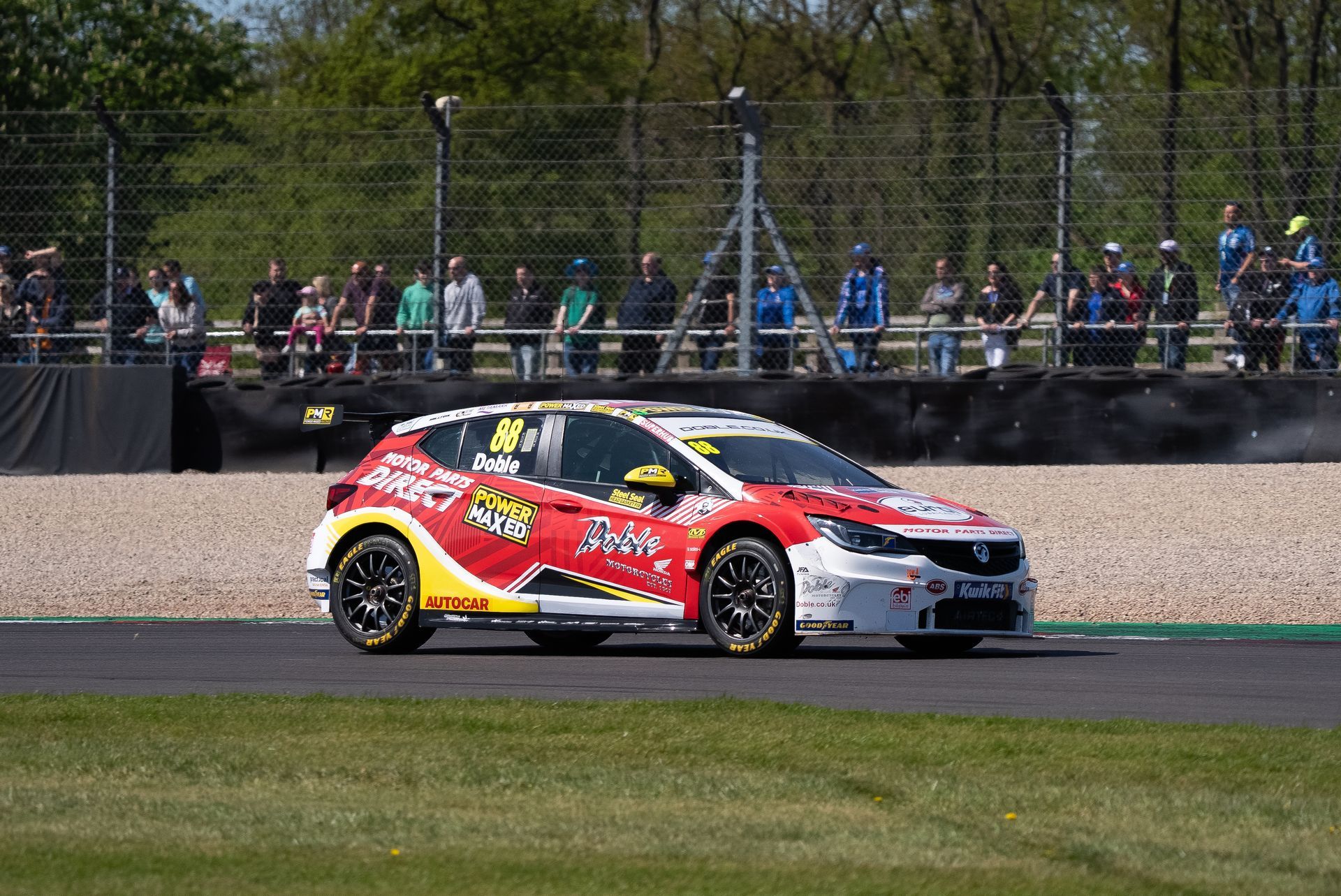 Race car on a track with spectators in the background. Red and yellow car racing on a green track.