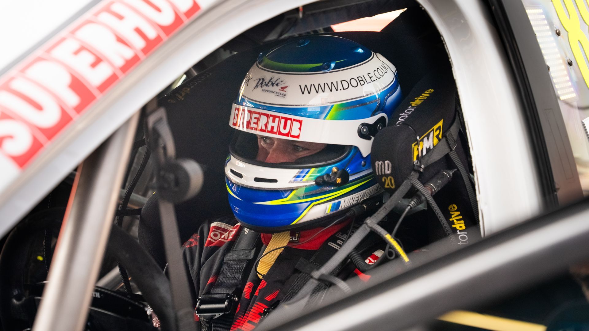 Race car driver in helmet, inside vehicle cockpit. Blue, white, and green helmet.