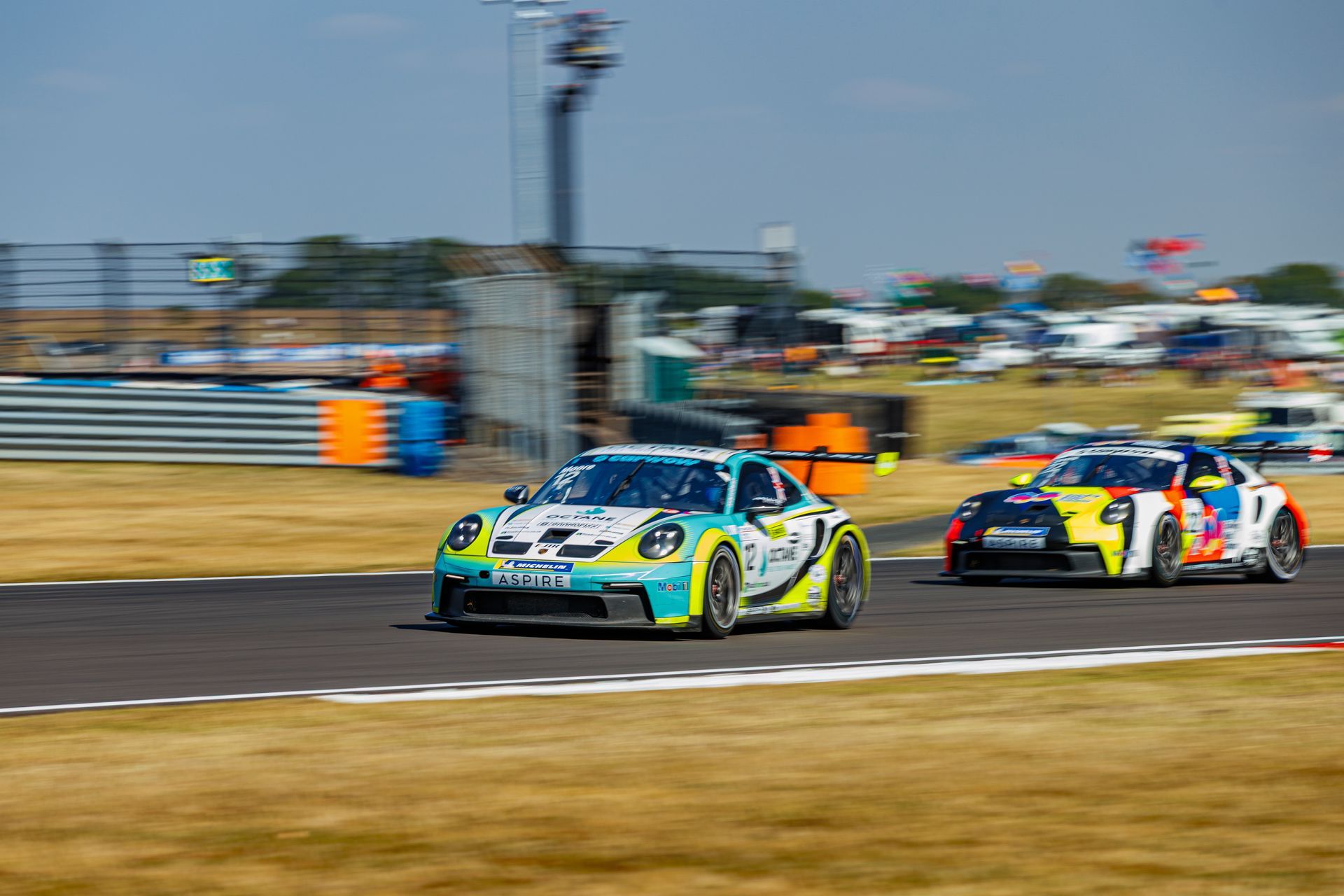 Two colorful race cars speed around a track, with one leading the other on a curve.