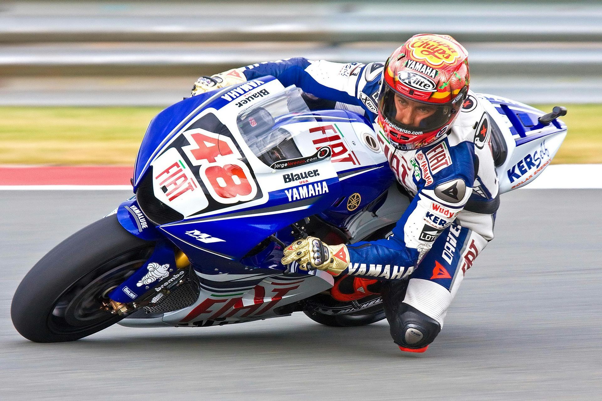 Motorcycle racer on a blue and white Yamaha, leaning into a turn on a track.
