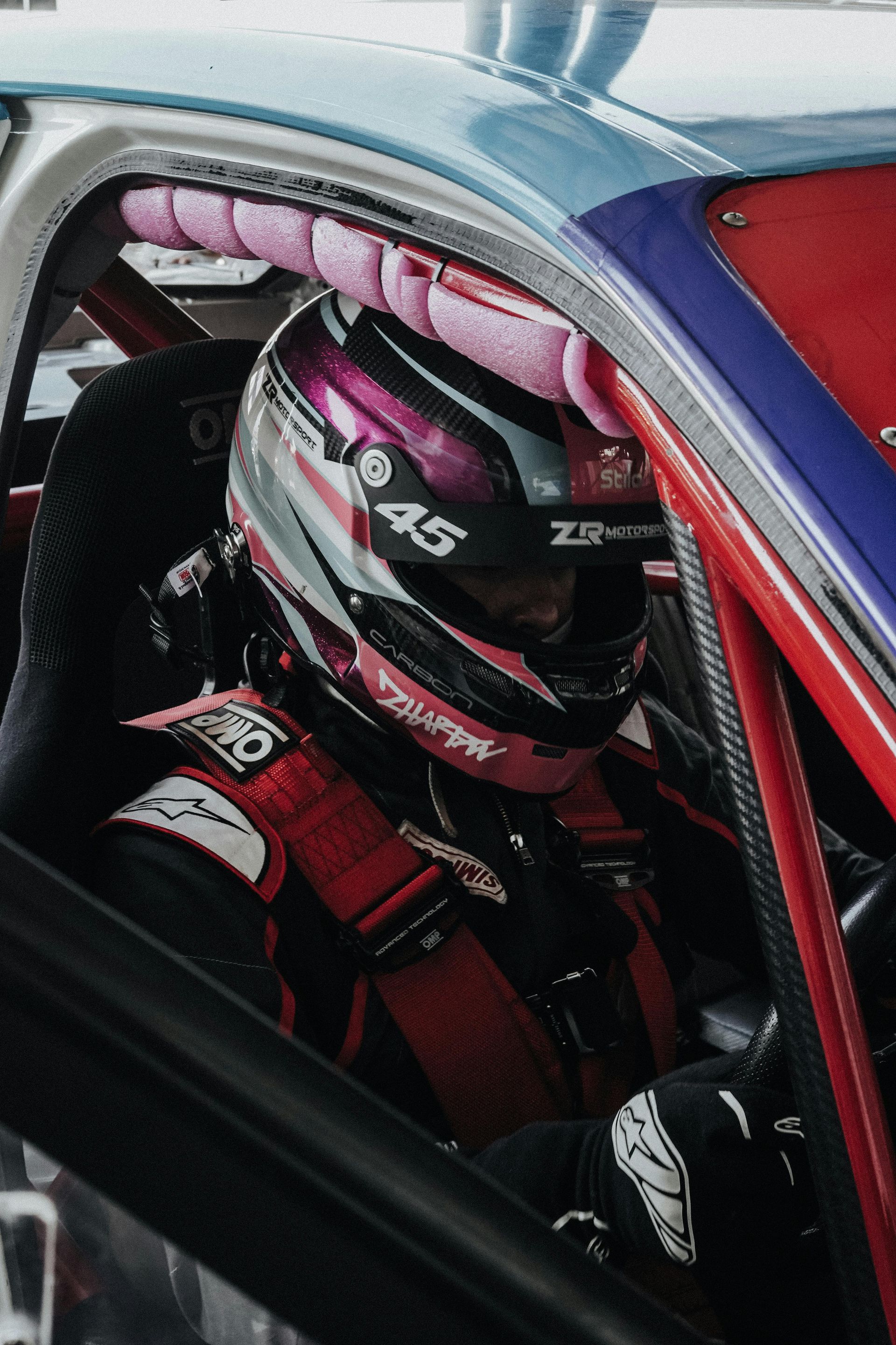 Race car driver in helmet, wearing safety gear, inside race car.