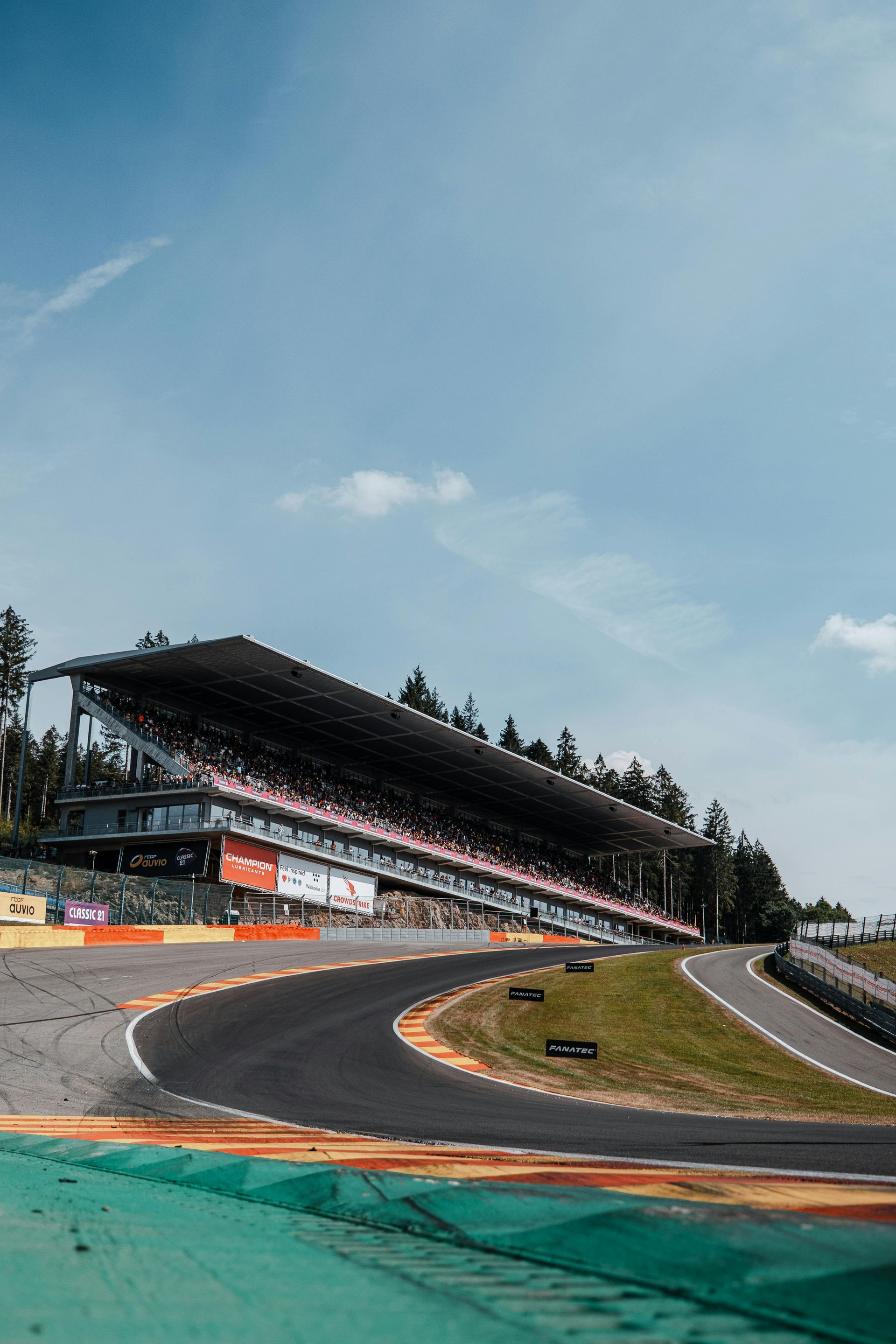 Race track with curved asphalt, spectator stands under blue sky.