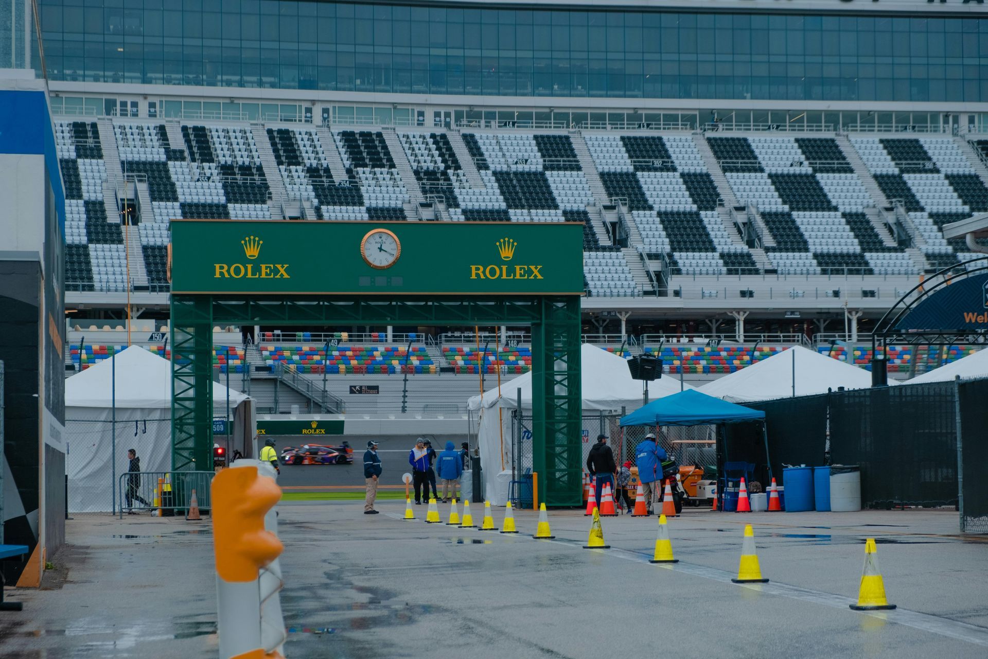 Race track entrance with green Rolex arch, cones, and a few people near check-in booths