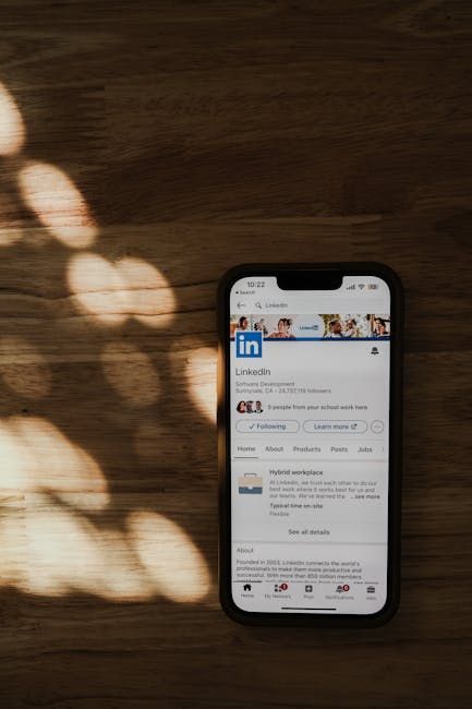 Smartphone displaying a LinkedIn profile page on a wooden surface with shadow.