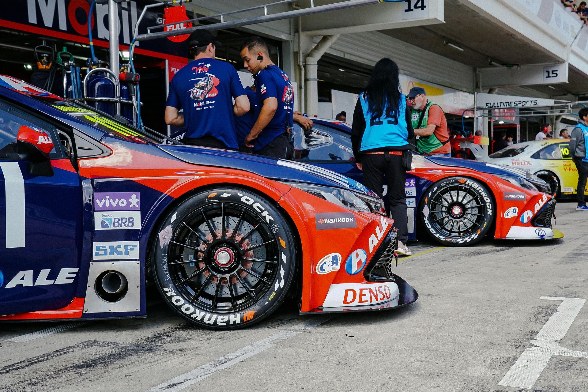 Red race car in pit lane with team members standing beside it.