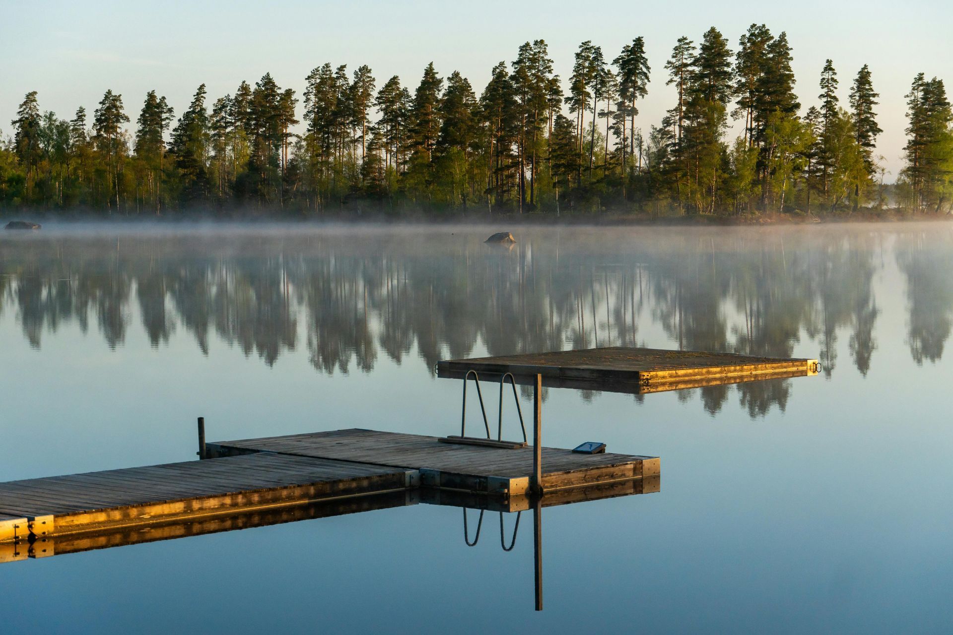 Wooden docks on a calm misty lake at sunrise, with pine trees reflected in the water.