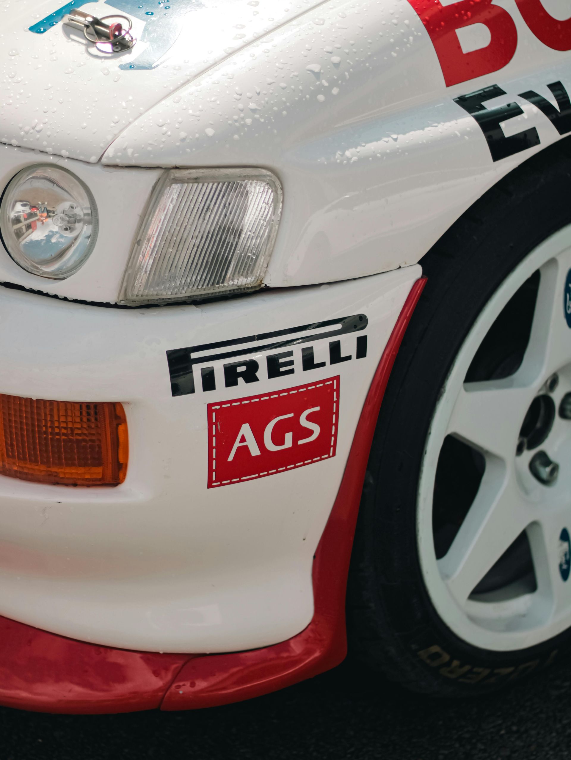 Close-up of white race car fender with Pirelli and AGS logos.