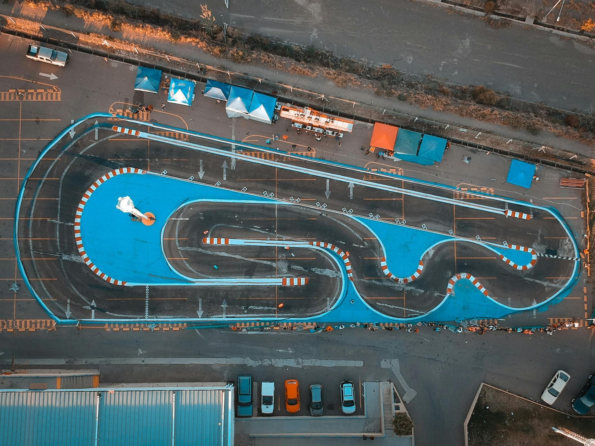 Aerial view of a go-kart track with blue borders and several parked cars.