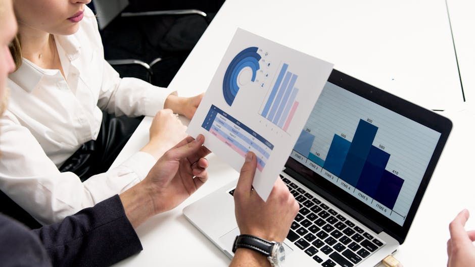 Two people reviewing charts and graphs on paper and laptop.