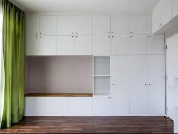 White built-in cabinets and shelving in a room with green curtains and dark wood flooring.