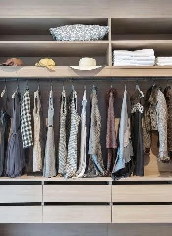 Open wardrobe with hanging clothes, hats, and folded linens on shelves above and drawers below