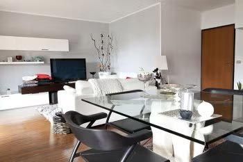 Modern living room with white sofa, glass dining table, TV, and wooden floor