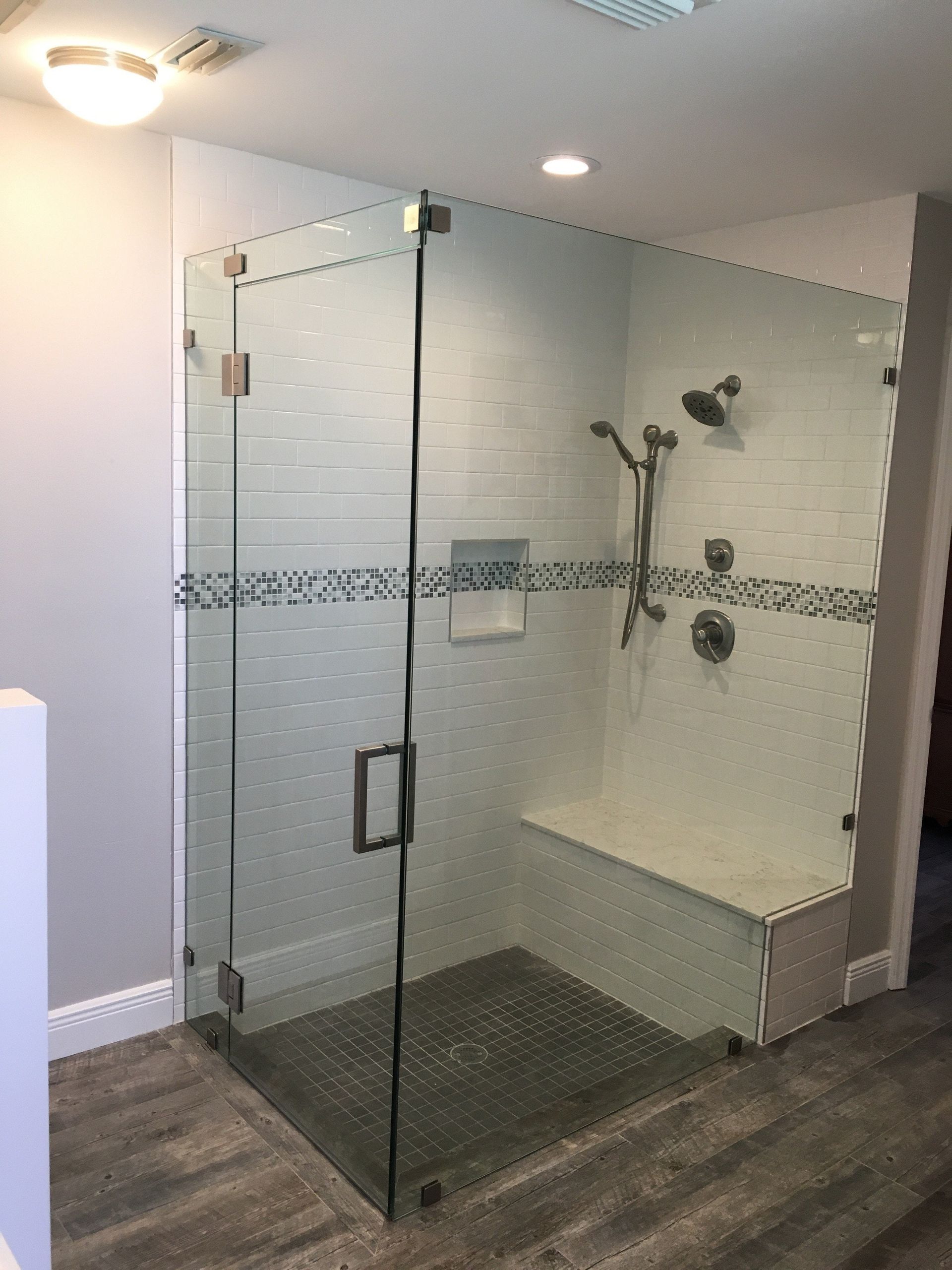 Glass walk-in shower with tiled wall, built-in bench, and chrome shower fixtures in a bathroom.