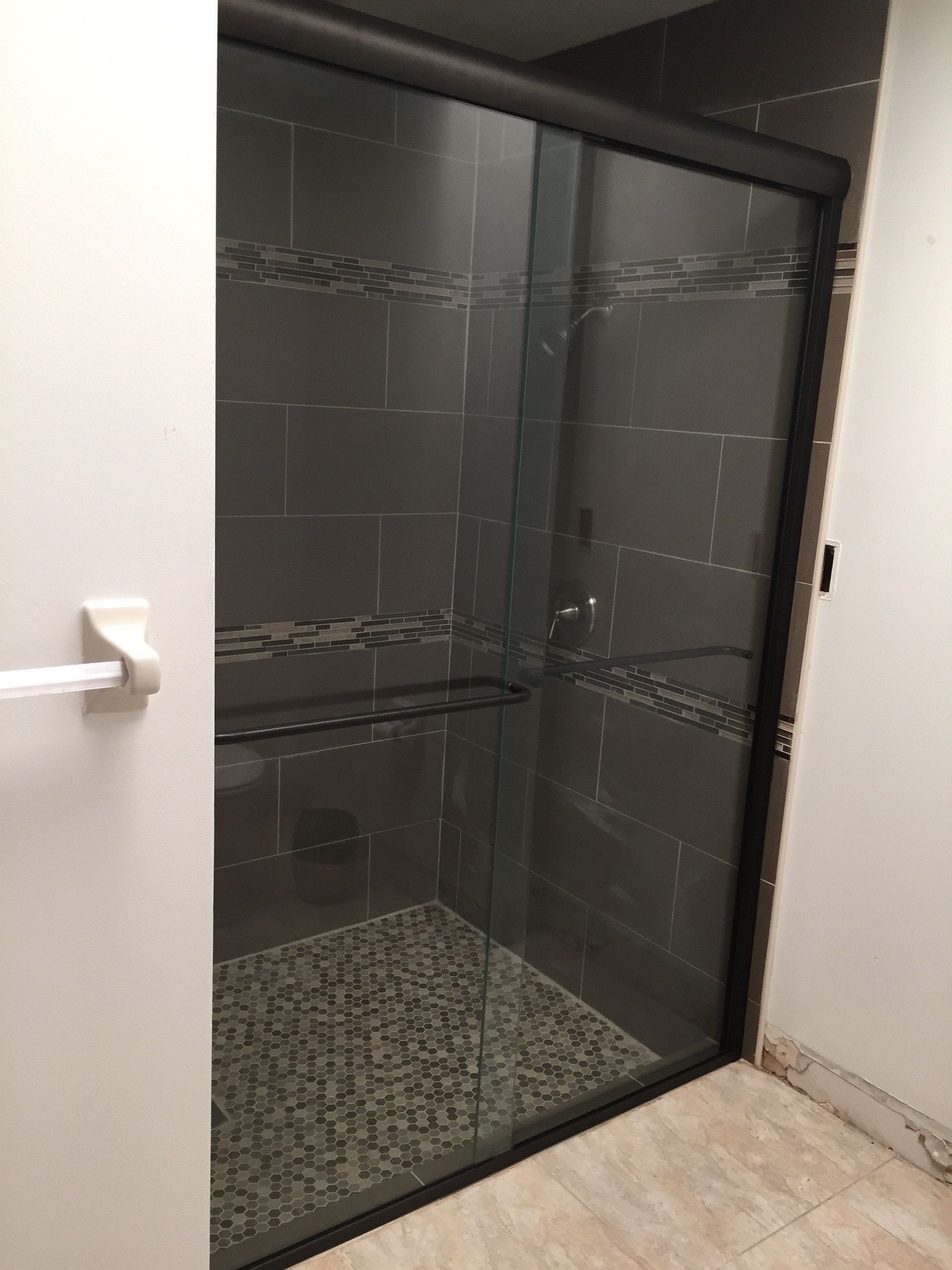 Glass shower stall with dark tile walls and a pebble-pattern floor in a bathroom