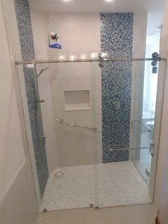 Glass shower enclosure with white tile walls and blue mosaic accent strip, seen through an open doorway